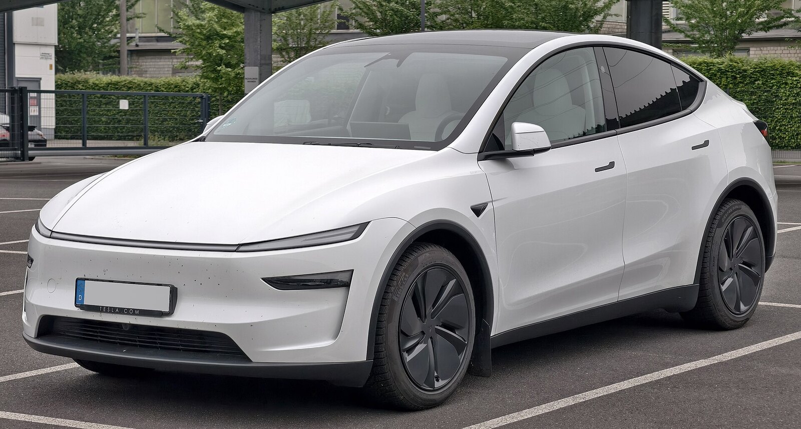 A white refreshed Tesla Model Y with German plates parked under a carport